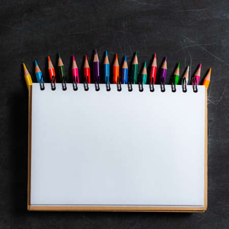 white notebook lies on a set of multi-colored pencils on a dark background