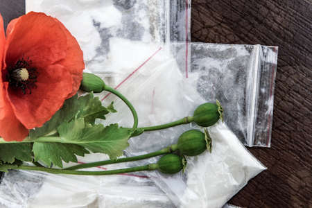flowers and heads of opium poppy next to packages of heroin, soft focus, tinting, selective...