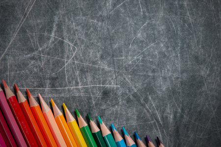 back to school: multicolored pencils lay on black chalkboard, short focus, partial blur