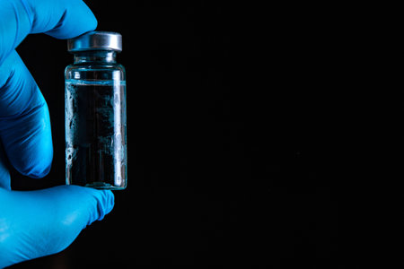 Sars-Kov-2 coronavirus vaccine in a transparent glass ampoule, covered with frost, on a dark...