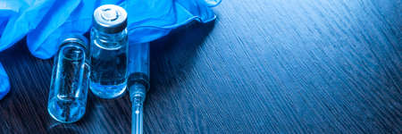 2 doses of Sars-Kov-2 coronavirus vaccine in transparent glass ampoules, covered with frost and a disposable syringe, on a dark background, short focus, toningの写真素材