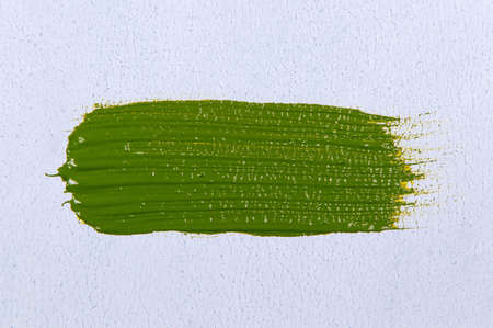 wide brush stroke with saturated bright light olive-green paint on a white background, close up