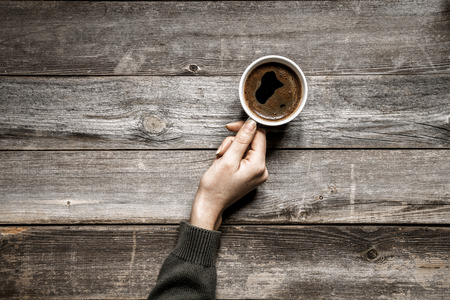 Woman hand drinking coffee on wooden tableの写真素材