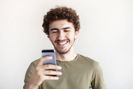 Portrait of a joyful smiling man in using mobile phone while standing isolated over white background