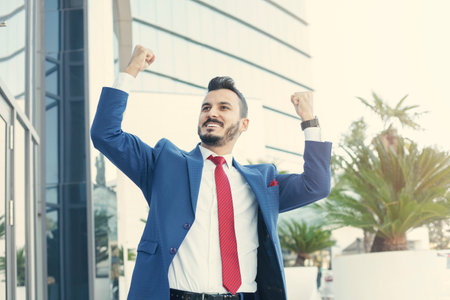 Cheerful businessman celebrating with fist in the air and hand in while standing.の写真素材