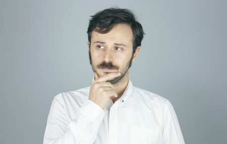 Thoughtful young man standing on gray background.