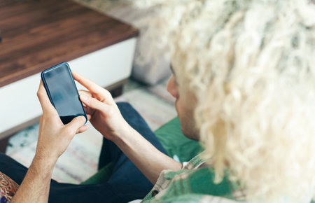 Young man on a couch at home, using mobile phoneの写真素材
