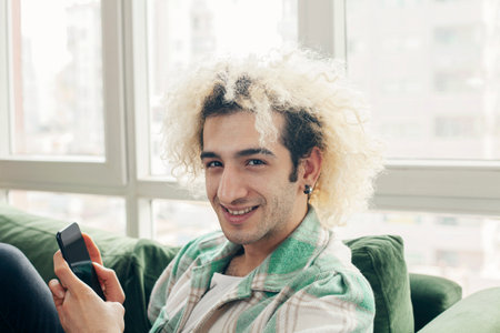 Young man on a couch at home, using mobile phoneの写真素材