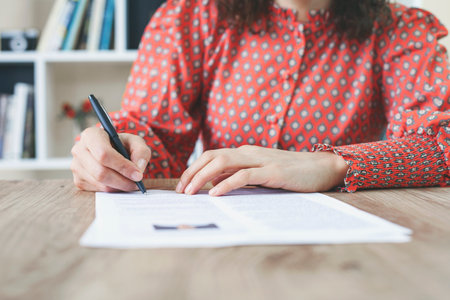 Woman at office desk signing a contract with shallow focus on signature.
