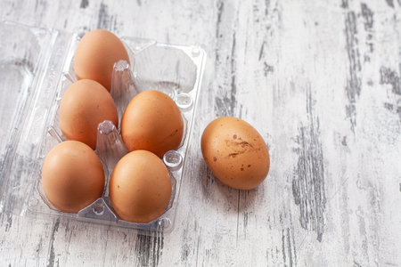 Close-up view of raw chicken eggs in egg box on white wooden background
