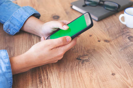 Cropped shot top view of businesswoman hands using smartphone mockup at the wooden office desk. Blank screen mobile phone for graphic display montageの写真素材