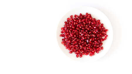Ripe pomegranate grains in a white  plate isolated on a white background. Top view, flat lay.の写真素材