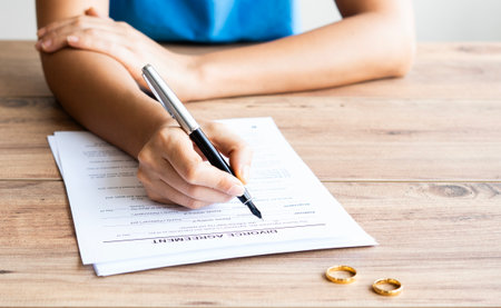 Human hand signing divorce contract, close-up. Wedding rings with marriage contract and judge gavel on a backgroundの写真素材