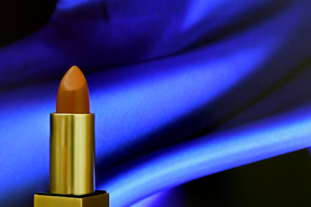 Close-up red brown lipstick  on blue shiny cloth background . Tube  and cover have gold color.の写真素材