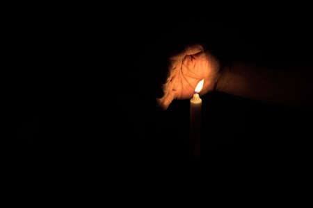 One hand protecting candle light from the wind. White candle burning in the darkness.の写真素材