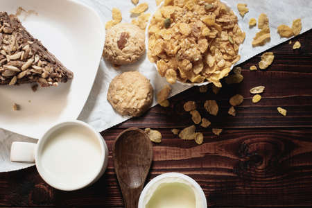 Simple breakfast on the wooden background with milk, yogurt , cake, cookies and corn flakes.Top viewの写真素材