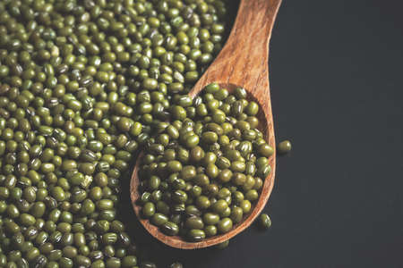 Close-up Mung beans in the wooden spoon on black backdrop.Health food components,has copy space...