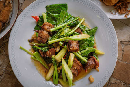 Stir fried kale vegetables with fried pork in the plate for breakfast or lunch or dinner,The food are kale vegetables with pork ,chili and garlic mixed together by heat.some menu on food tableの写真素材