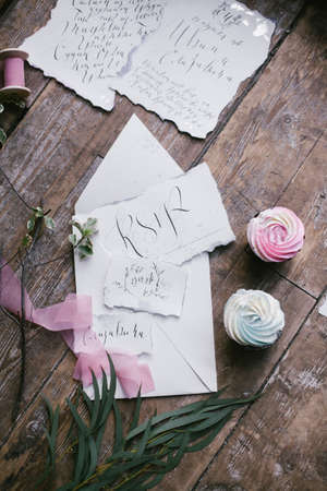 Graphic arts of beautiful wedding calligraphy cards with two mini cakes and pink chiffon ribbon on wood background.の写真素材