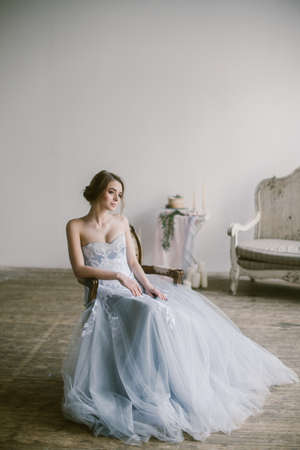 Portrait of young beautiful modern bride in grey lace dress sitting in a sofa.の写真素材