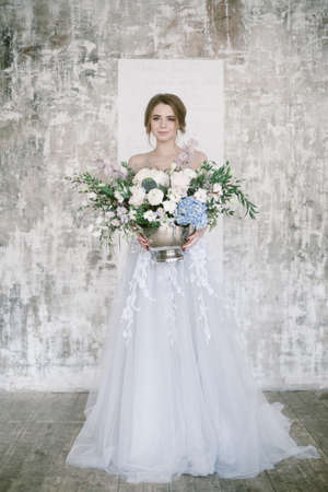 Beautiful floral composition in silver bowl in hands of young smiling bride.の写真素材