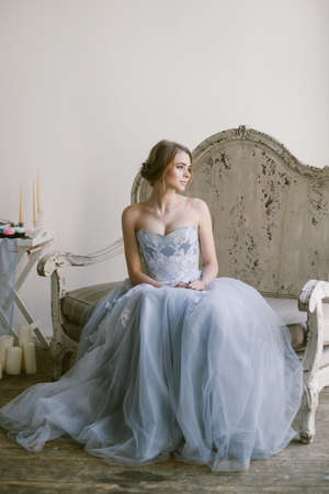 Portrait of young beautiful modern bride in grey lace dress sitting in a sofa.の写真素材