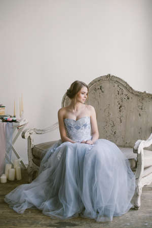 Portrait of young beautiful modern bride in grey lace dress sitting in a sofa.の写真素材