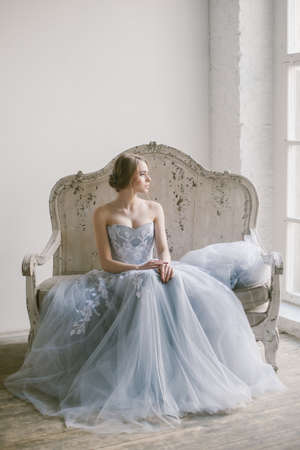 Portrait of young beautiful modern bride in grey lace dress sitting in a sofa.の写真素材