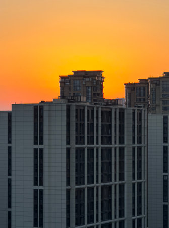 Beautiful sunset over modern buildings in an urban landscape showcasing vibrant orange and yellow tones near duskの写真素材