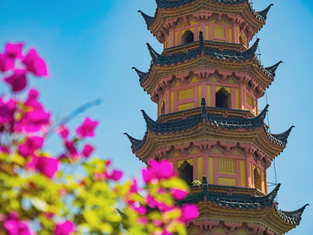Colorful pagoda surrounded by vibrant flowers in sunlight captures serene beauty of the garden during daytimeの写真素材