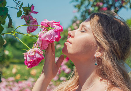 Young woman enjoys a sunny day among blooming roses in a vibrant garden settingの写真素材