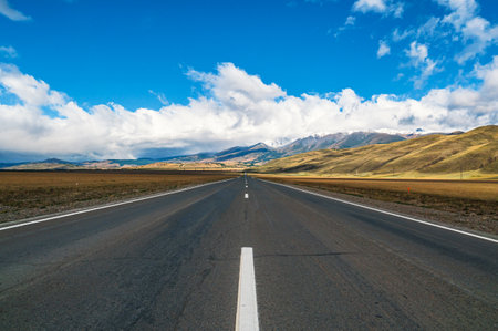 Breathtaking view of an open road leading to majestic mountains in Gorny Altay during a clear day with scattered clouds.の写真素材