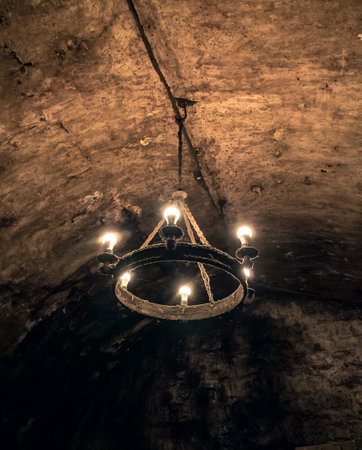 Old chandelier hanging from a rough stone ceiling in a dimly lit historic cellarの写真素材