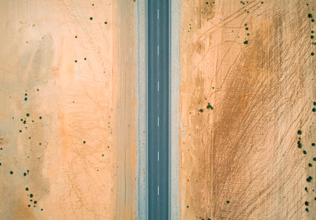 Stretch of highway through barren desert landscape under clear blue sky in remote locationの写真素材