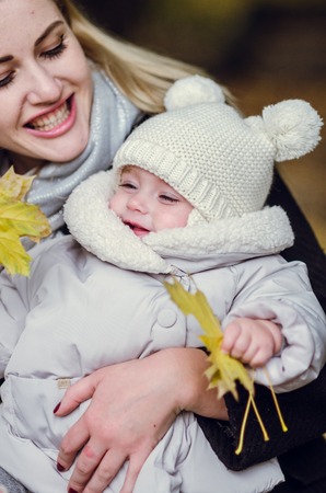 Mother and daughter play in autumn park. Parent and child walk in the forest on a sunny fall day. Toddler girl picking golden leaves. Mom hugging kid.の写真素材