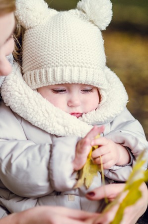 Mother and daughter play in autumn park. Parent and child walk in the forest on a sunny fall day. Toddler girl picking golden leaves. Mom hugging kid.の写真素材