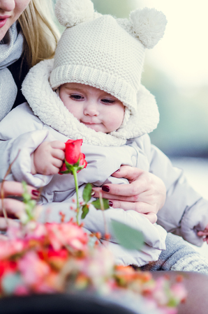 Mother and daughter sitting on a bench in the park and hugging. Toddler picking a flower.の写真素材