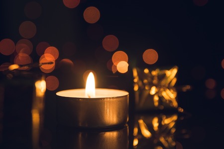 Tea Light Candle burning with bokeh lights on black backgroundの写真素材