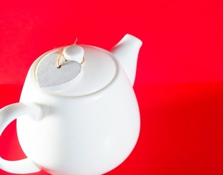 white teapot with heart tied with a cord isolated on red background. Love teaの写真素材