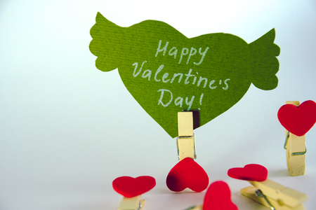 Valentines day concept. Green paper heart with wings and congratulation fixed on a clothespin and 4 heart shape clothespins on white background.の写真素材