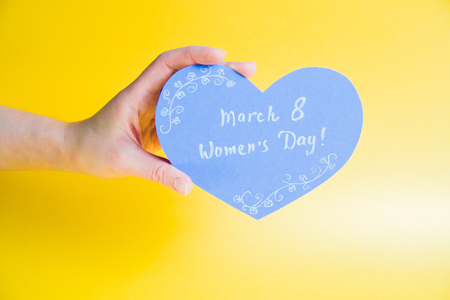 Female hand holding blue paper heart on golden background - Happy Womens Dayの写真素材