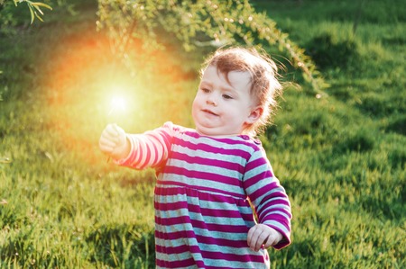 Happy little toddler girl walk outdoors on a sunny day holding flower. Spring time, green grass.の写真素材