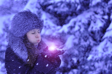 Happy girl with fur cap and gloves blowing snowflakes in the winter cityの写真素材