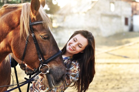 Beautiful young female walking and caressing her brown horse in a countrysideの写真素材