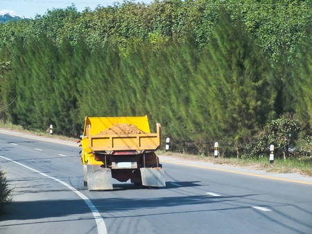 yellow truck containing dirt driving on a roadの写真素材