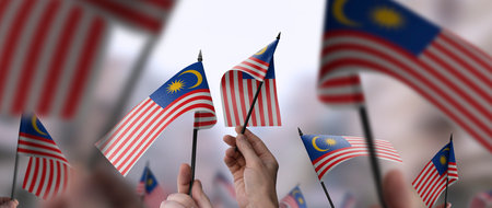 Malaysia flags in their hands on a blurred urban backgroundの写真素材