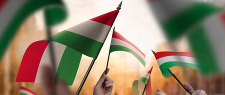Hungary flags in their hands on a blurred urban background. The photo illustration was created...