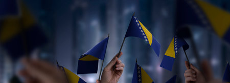Bosnia and Herzegovina flags in their hands on a blurred urban backgroundの写真素材