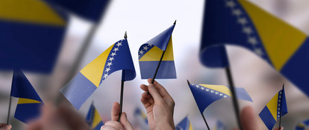 Bosnia and Herzegovina flags in their hands on a blurred urban backgroundの写真素材