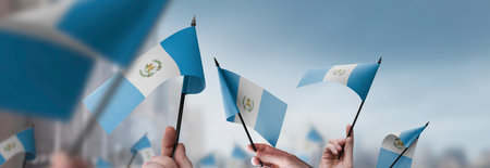 Guatemala flags in their hands on a blurred urban background. The photo illustration was created without the use of artificial intelligence, only using Photoshop.の写真素材